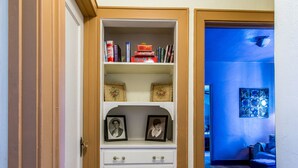 A hallway with a white storage unit containing books and framed photos.