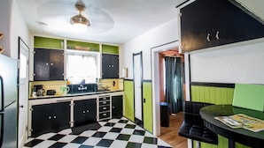 A compact kitchen with a checkered floor, green and black cabinets, a sink, and a ceiling fan.