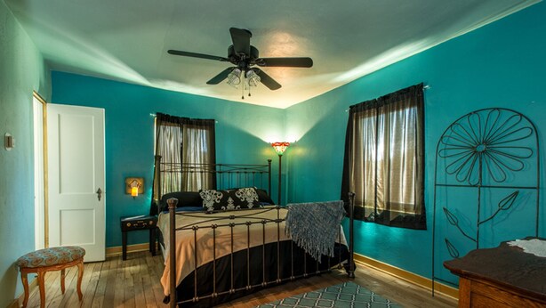 A bedroom with a bed, a nightstand, a chair, a floor lamp, and a decorative wall piece.