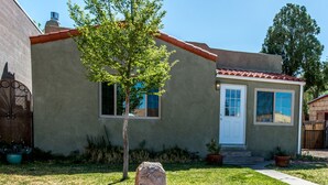 A house with a stucco exterior, a tiled roof, and a front yard with a tree and rocks.