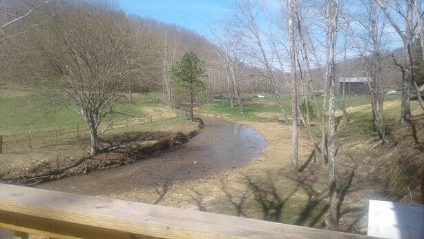 Un paysage rural avec un ruisseau sinueux, des arbres et une clôture en bois.