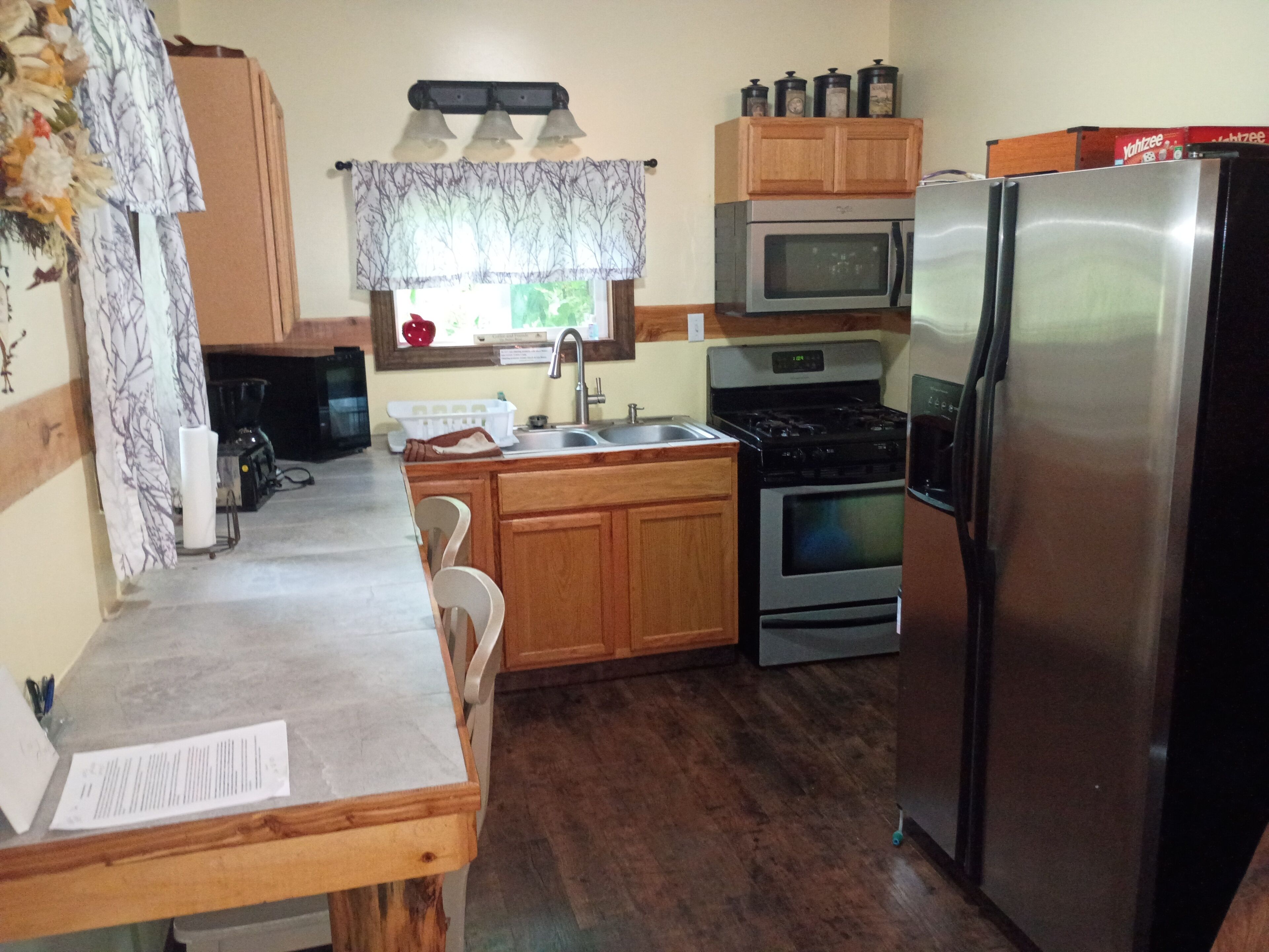 A kitchen with wooden cabinets, a stainless steel refrigerator, a microwave, an oven, and a sink.