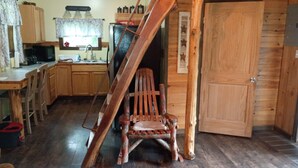 Un intérieur rustique avec un escalier en bois, un coin repas avec des meubles en bois et une cuisine dotée de placards en bois et d’un réfrigérateur.