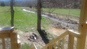 Une terrasse en bois donnant sur un champ verdoyant, avec un ruisseau qui le traverse.