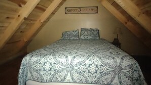 Une chambre avec un plafond en pente, un lit avec une literie à motifs et un plancher en bois.