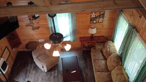 L’intérieur d’un chalet accueillant, avec un plafond en bois, un canapé, un fauteuil, une table et un ventilateur de plafond.