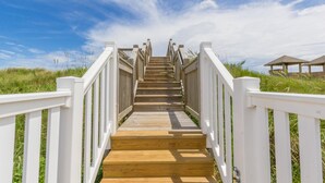 Een houten trap met witte leuningen die naar een strand loopt.