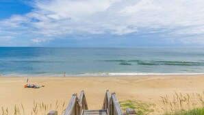 Een strand met een houten looppad dat naar het water leidt, zandstrand en heldere lucht.