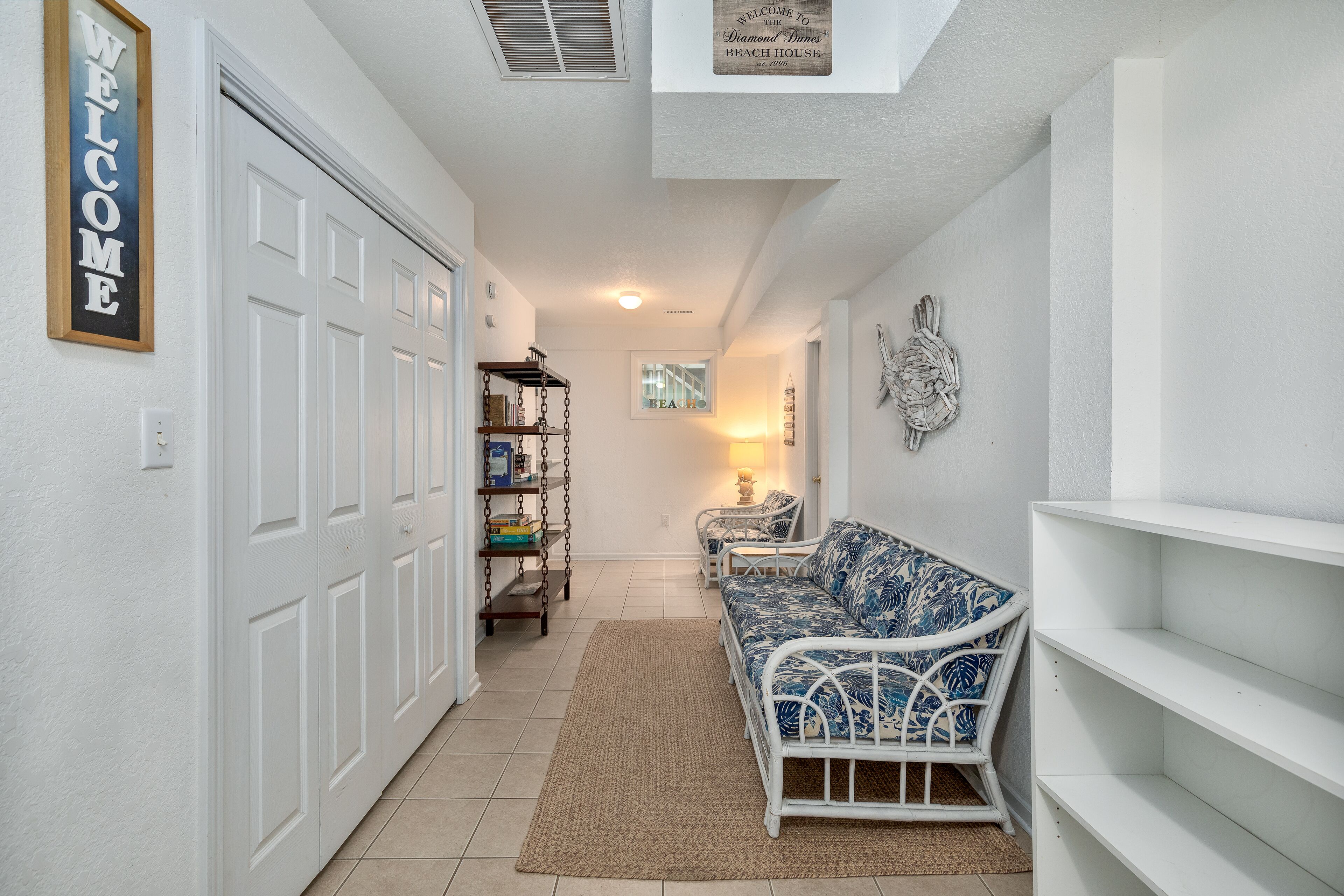 A hallway with a white door, a welcome sign, a wicker sofa, and a wall-mounted decorative piece.