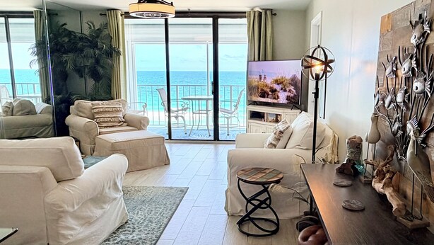 Un ampio soggiorno con una grande TV, comodi posti a sedere, un tavolino in legno e vista sull'oceano attraverso ampie finestre.