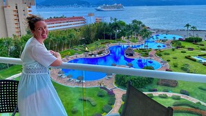 Un balcón con vistas al área de piscina de un resort, que incluye varias piscinas y sillones de descanso.