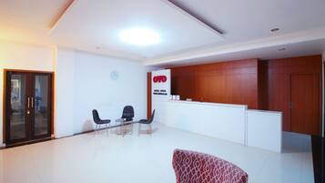 A hotel reception area with a reception desk, two chairs, a patterned sofa, and a wooden reception counter.