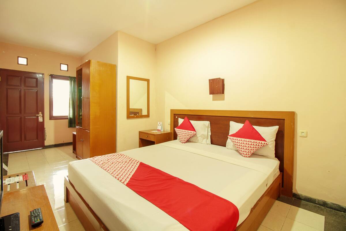 Ein Hotelzimmer mit einem großen Bett, einem Holzkopfteil, einem Nachttisch mit Lampe, einem Spiegel an der Wand und einer Tür zum Badezimmer.