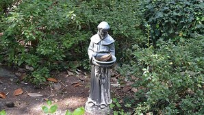 A statue of a figure holding a bowl, surrounded by dense greenery.