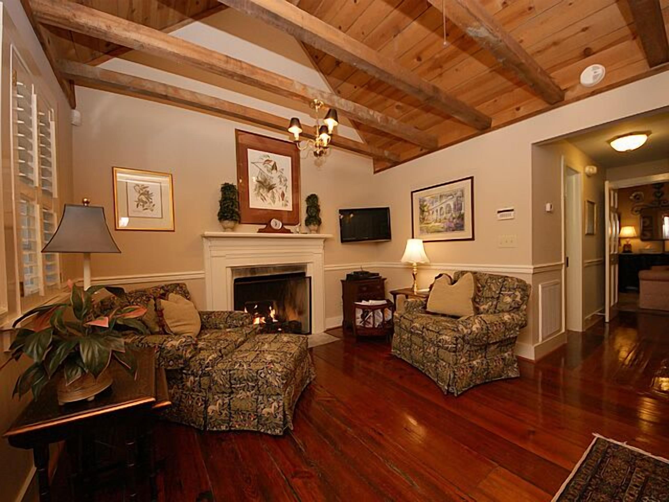 A cozy living room with a fireplace, two patterned armchairs, a television, and framed artwork on the walls.