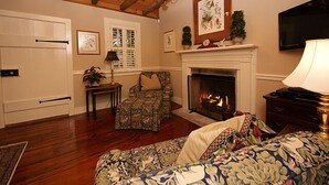 A cozy living room with a fireplace, wooden ceiling beams, a sofa, a chair, and a television.