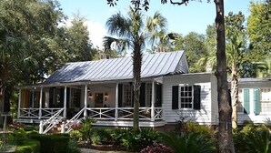 A white house with a porch, surrounded by tropical plants and a stone pathway.