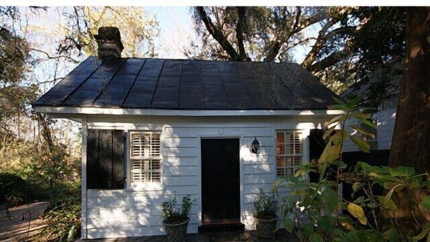 A small white house with a dark roof, a front door, and two windows with shutters.