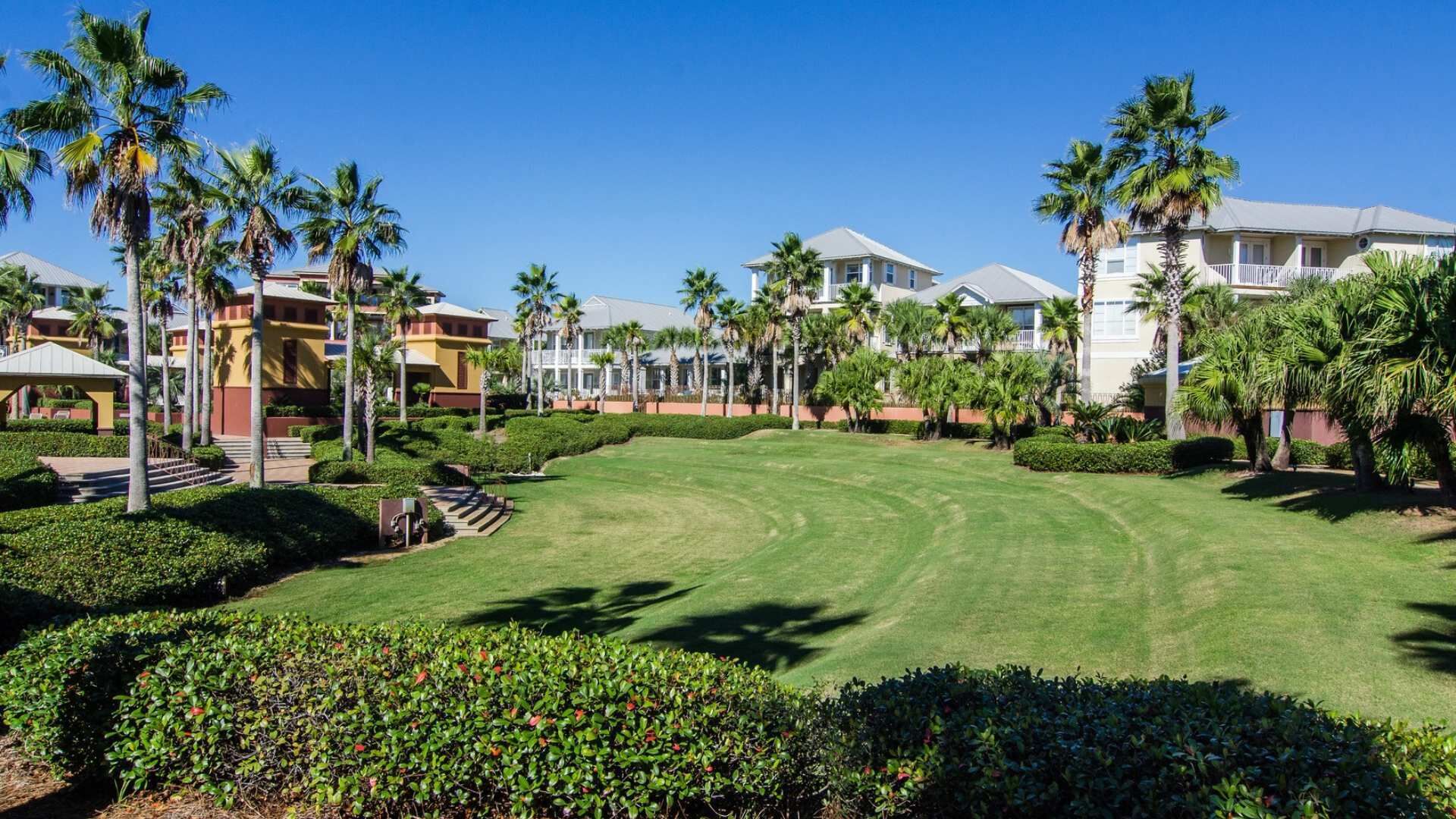 Un campo de golf bien cuidado con césped impecable y palmeras, rodeado de edificios tipo resort con balcones.