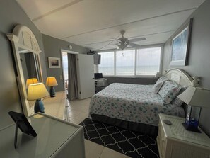Una camera da letto con un letto, comodini, una scrivania, una sedia, una ventola a soffitto e una finestra con persiane.