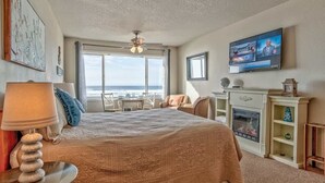 Een hotelkamer met een groot bed, een televisie, een open haard en uitzicht op de oceaan.