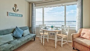 Een kamer met uitzicht op de oceaan, een plafondventilator, een tafel met stoelen, een bank en een bord aan de muur.