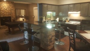 A kitchen with a central island, bar stools, and a dining area with chairs.