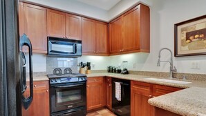 A kitchen with wooden cabinets, a black stove, a microwave, and a dishwasher. - Desert Tranquility 2 | 2BR Legacy Villa (La Quinta)