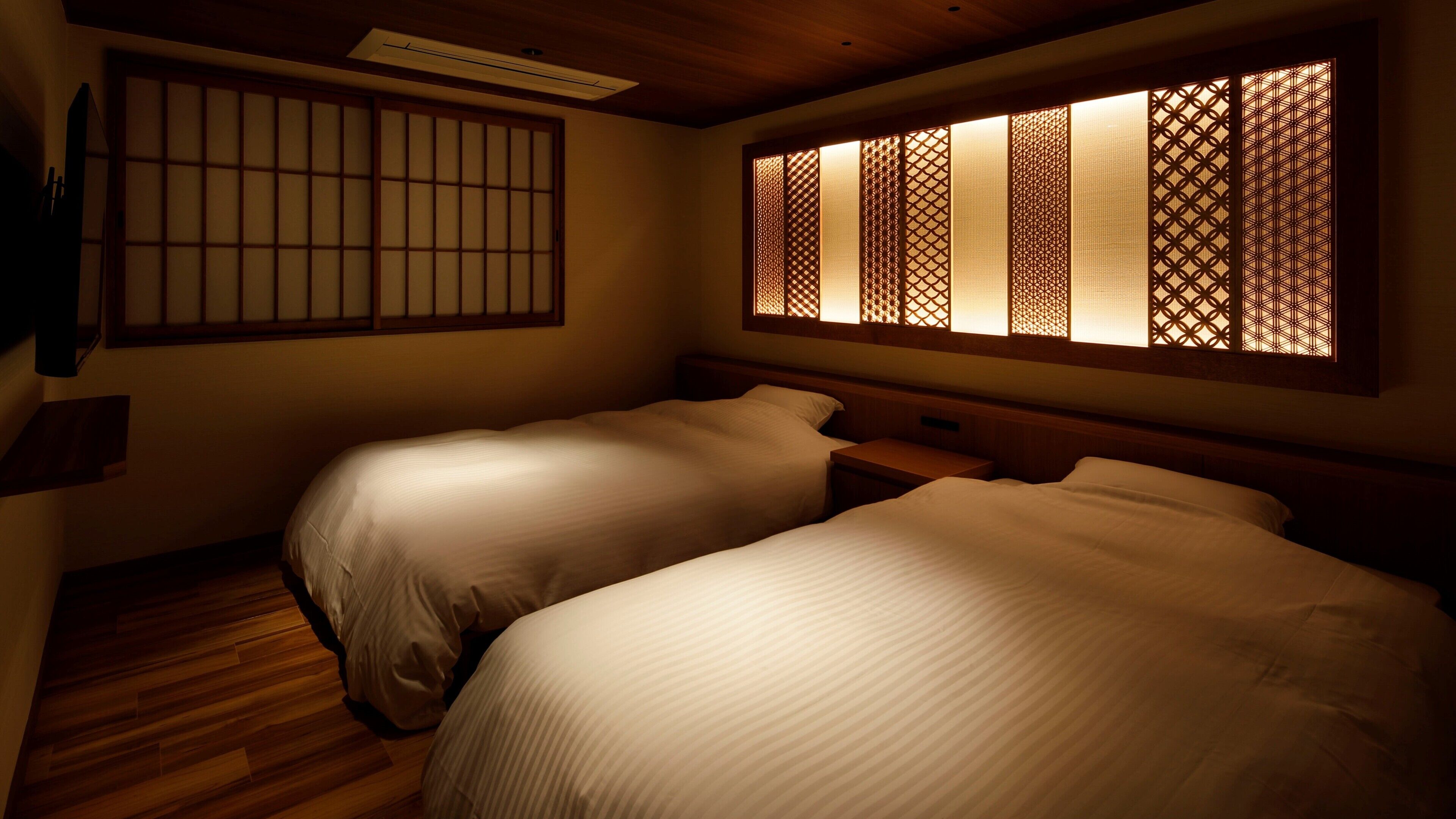 A traditional Japanese-style room with two beds, wooden flooring, and sliding doors with intricate patterns.