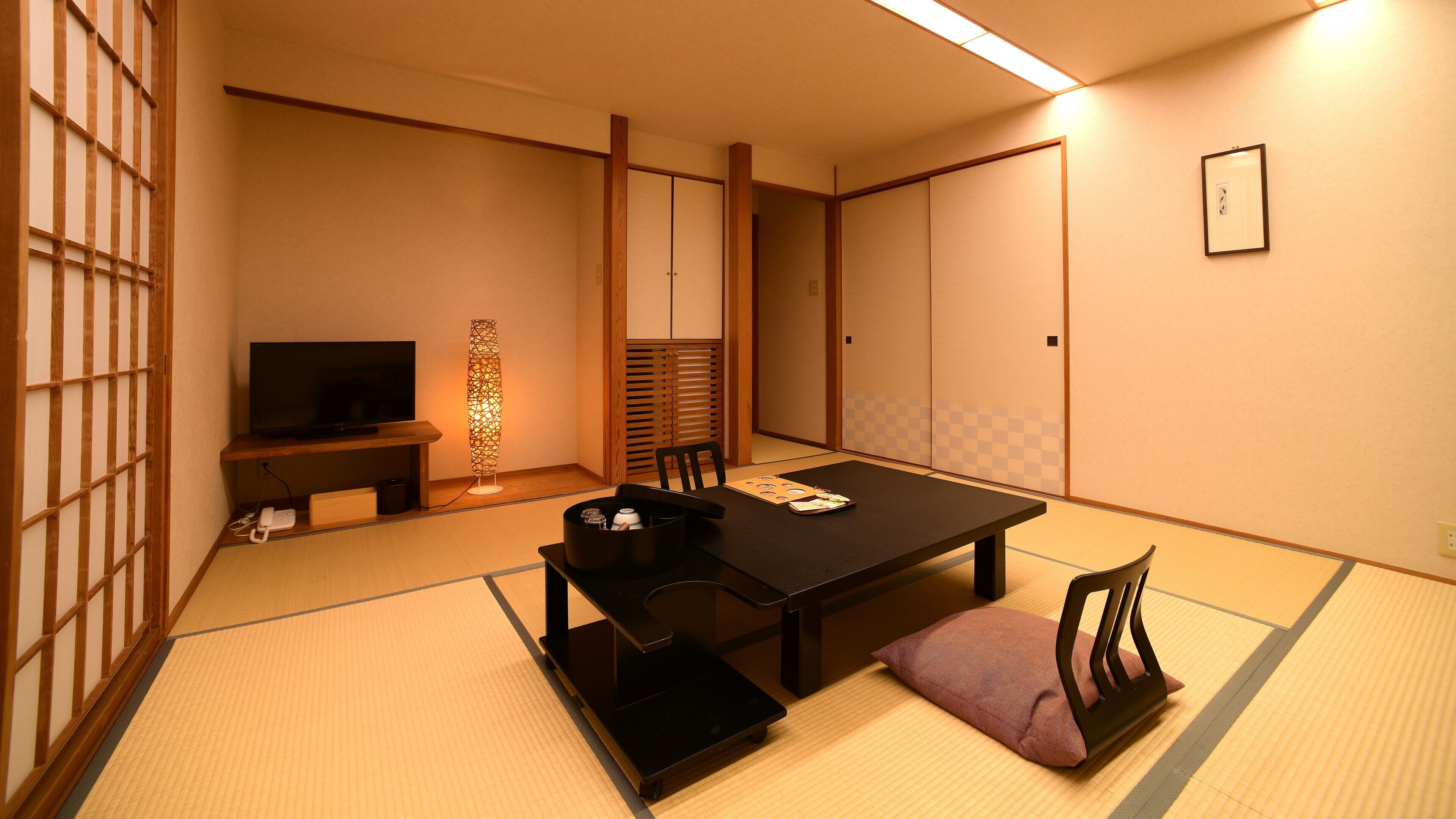 A traditional Japanese room with tatami flooring, a low table, a sofa, a television, and sliding doors.