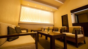 A hotel room with a sofa, armchairs, a coffee table, and a large window with a view of a building. - Sadasuke (Kami)