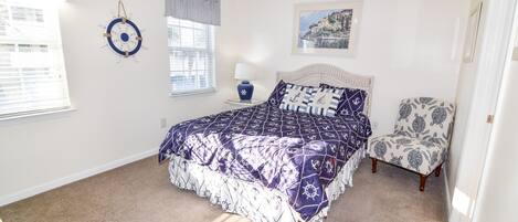 A bedroom with a bed, a chair, a wall clock, a lamp, and a framed picture.
