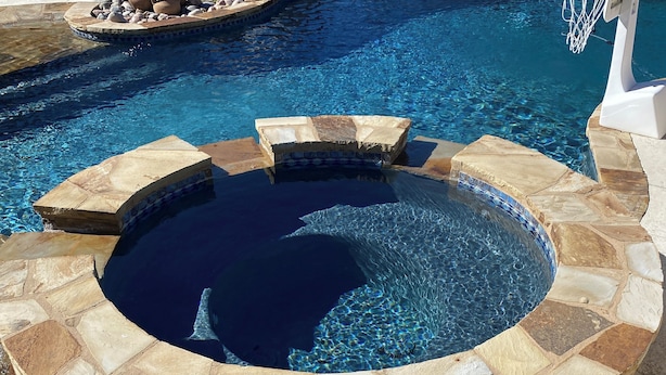 Un jacuzzi de piedra circular con un aro de baloncesto, rodeado por una terraza de piedra.