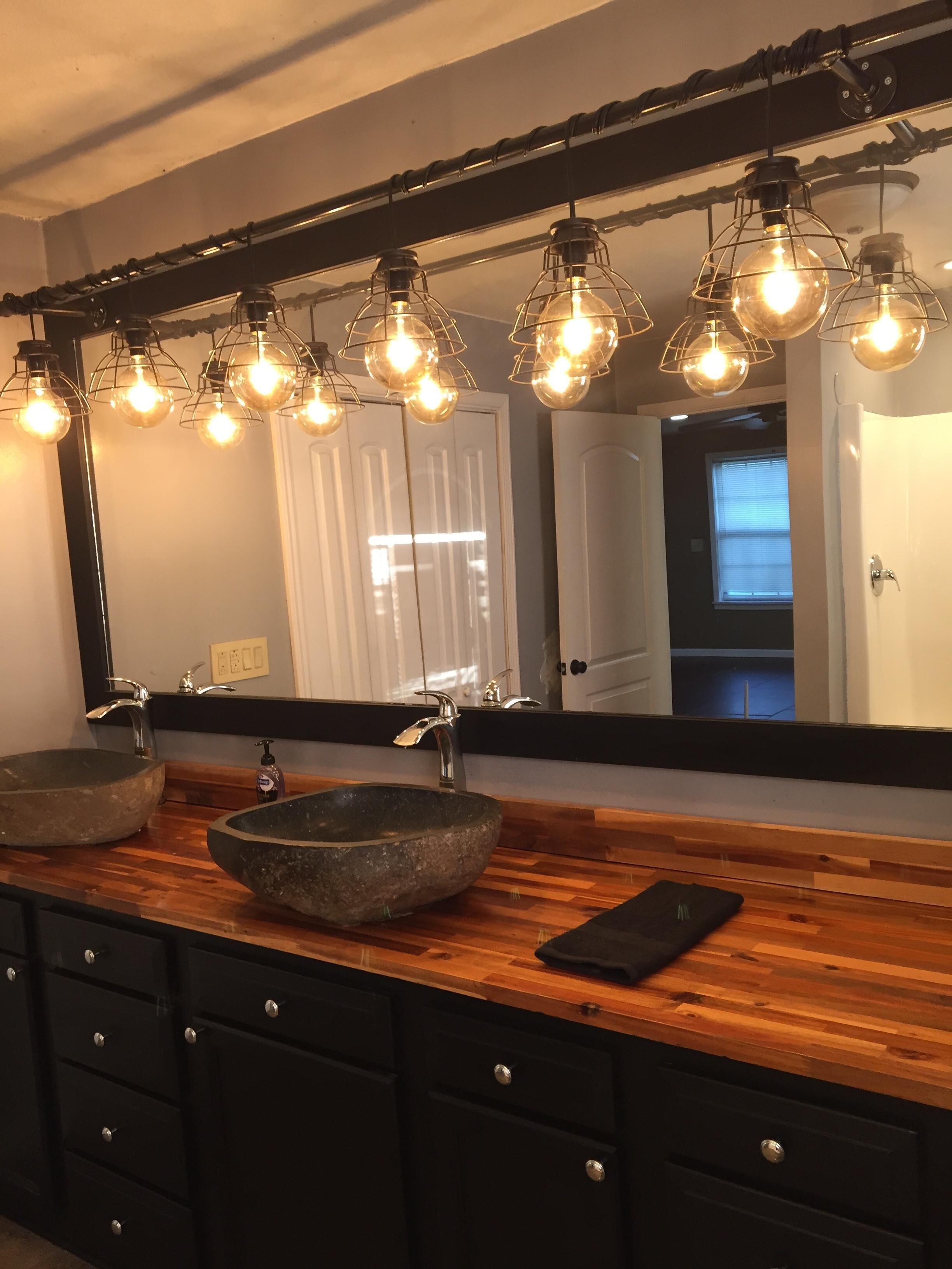 A bathroom with a large mirror, two vessel sinks, wooden vanity, and pendant lighting.