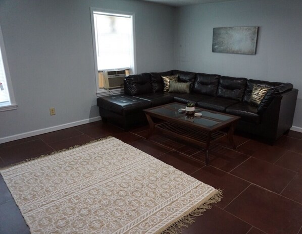 A living room with a dark leather sectional sofa, a glass coffee table, and a patterned rug.