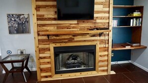 A living room with a wooden wall-mounted TV, a fireplace, and a bookshelf.