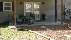 A covered patio with a table and chairs, a door with glass panels, and a small garden area with mulch and stepping stones.