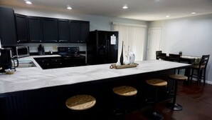 Una cocina moderna con armarios oscuros, una isla grande con taburetes y un comedor con sillas.