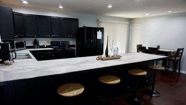 A modern kitchen with dark cabinets, a large island with stools, and a dining area with chairs.