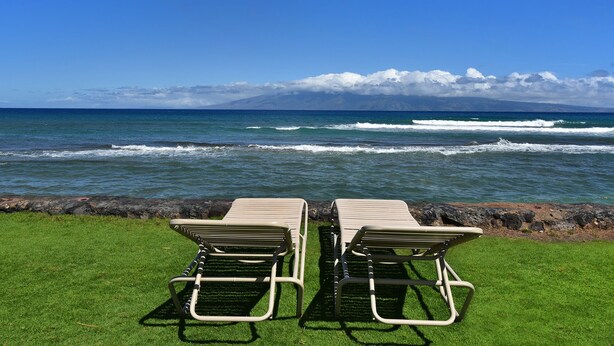 Dos sillones de relax mirando una playa con olas y una montaña al fondo.