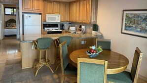 Cocina compacta con armarios de madera, microondas, estufa y comedor con una mesa redonda y sillas.