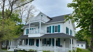 A two-story house with a porch, white siding, and green shutters. - Historic Petunia Cottage: Large Renovated Victorian Excellent In-town Location (Bar Harbor)