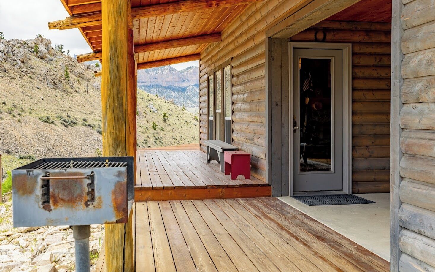 A wooden cabin with a deck, a grill, and a bench.