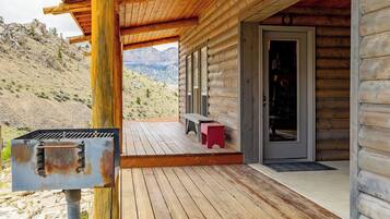 A wooden cabin with a deck, a grill, and a bench.