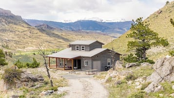 A rustic cabin with a porch, a covered patio, and a view of snow-capped mountains.