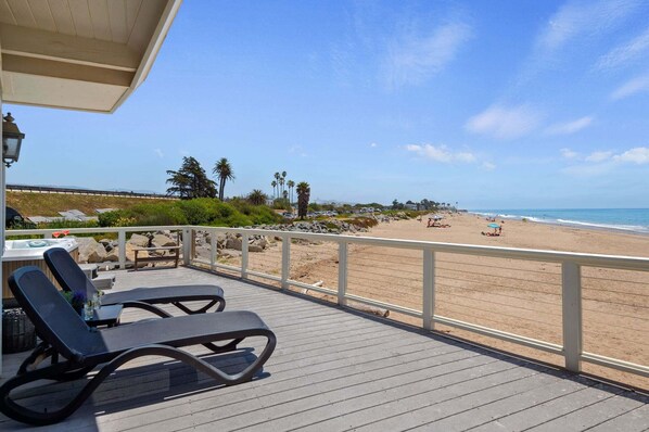 A wooden deck with lounge chairs overlooking a beach with a clear sky. - Beautiful Oceanfront Home with Jacuzzi (Carpinteria)