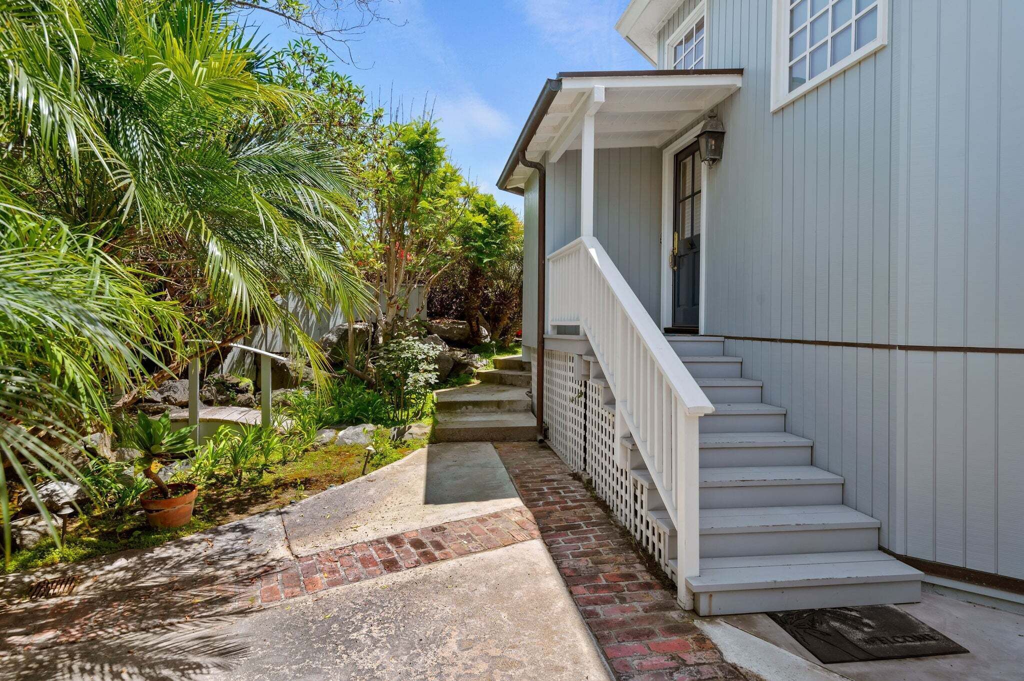 A house with a porch, steps leading to a door, and a garden with plants and a pathway.