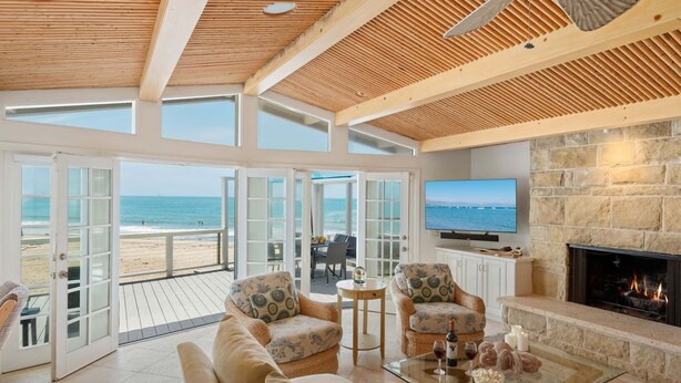 A spacious living area with a large TV, a fireplace, and a view of the beach. - Beautiful Oceanfront Home with Jacuzzi (Carpinteria)