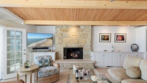 A living room with a stone fireplace, a television, and a sofa. - Beautiful Oceanfront Home with Jacuzzi (Carpinteria)
