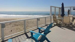 A beachside deck with chairs and tables, a fence, and a view of the ocean. - Beautiful Oceanfront Home with Jacuzzi (Carpinteria)